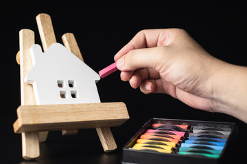 White house model on the realistic wooden easel with hand of Interior designer holding chalk color and black background.