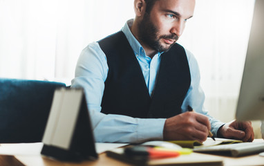 Bearded businessman writes in notebook at home workplace. Manager working at office. Finance consultant thinking looking in monitor computer, online internet work process concept, social distance