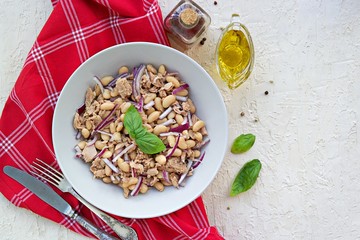 Hearty salad with boiled beans, canned tuna and purple onions in a gray plate on a light concrete background. Dressed with olive oil. Italian food.