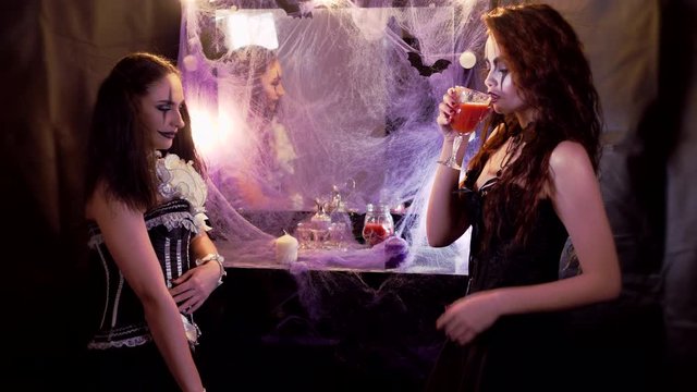 Makeup of the actor. The girl in the image of the devil's Bride takes a glass of red liquid from the clown's girl.