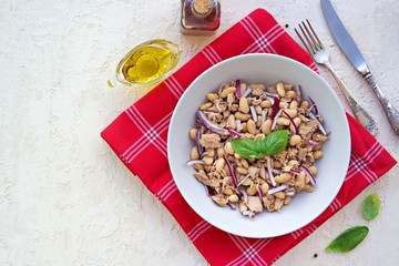 Hearty salad with boiled beans, canned tuna and purple onions in a gray plate on a light concrete background. Dressed with olive oil. Italian food.