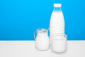 on a white table stands a bottle and glasses and a decanter with milk on a blue background. High calcium content. Healthy drink.