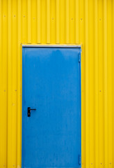 Blue close metal door on a yellow wall.