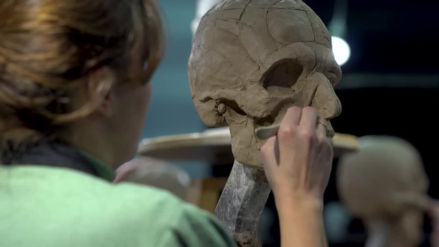 Woman sculptor at work on a sculpture of a human head. The process of restoring the shape of the wings of the nose. Side view. Close up view.
