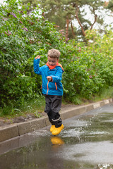 Toddler boy jumping in a puddle in yellow waterproof boots. Fun on the street. Tempering in summer....