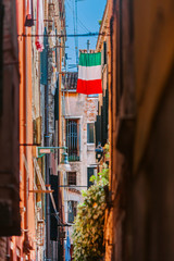 A narrow street in Venice, Italy. The Italian flag weighs between neighboring houses. Tourist destination Italy.
