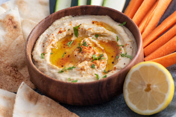 Homemade hummus with olive oil, herbs and paprika in a wooden bowl. with vegetable and bread dips.