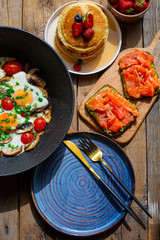 Beautiful breakfast on a wooden table.Fried eggs with mushrooms and green onions.Bright eggs with tomatoes, mushrooms and onions.Pancakes for breakfast with berries and syrup.Sandwiches with avocado 