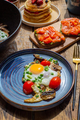 Beautiful breakfast on a wooden table.Fried eggs with mushrooms and green onions.Bright eggs with tomatoes, mushrooms and onions.Pancakes for breakfast with berries and syrup.Sandwiches with avocado 