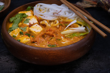 Vegan thai noodles and tofu red curry served in  wooden bowl on dark table