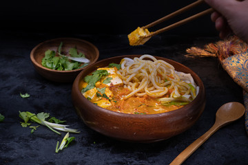 Chopsticks holding thai  tofu cooked with noodles in red curry