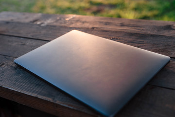 Single laptop computer on a wooden table. Laptop lying on a wooden table behind which is sunset. Laptop. Free space for your text.