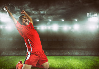 Soccer striker in red uniform rejoices for the victory at the stadium