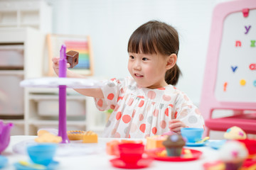 Obraz na płótnie Canvas toddler girl prerend play preparing tea party at home