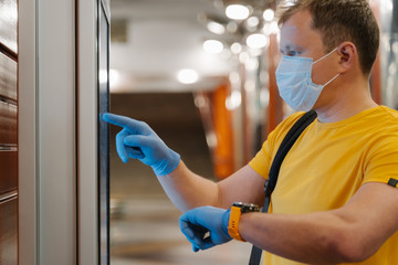 Profile shot of man checks time on watch, uses touch screen in protective rubber gloves, avoids spreading coronavirus, pandemic time, wears medical mask. Health care, quarantine, virus outbreak
