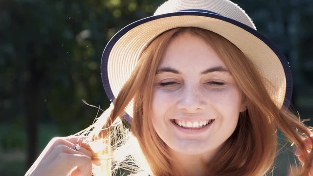 Portrait of pretty positive teenage girl with red hair wearing straw hat and pink earphones smiling happily in camera.