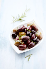 Green and Kalamata olives with fresh rosemary on bright wooden background. Close up.