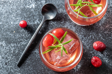 Delicious refreshing cocktail with vodka, cranberry juice and rosemary on black stone table top view.