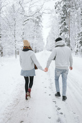 Fototapeta na wymiar Young lovers walk in the winter park. A pair of people walks into the distance on a snowy road