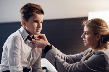 A close up picture of a mother fixing her son's tie in the bedro