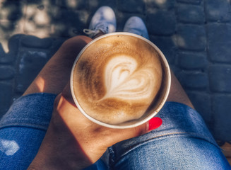 In female hands a paper cup with coffee with foam in the form of a heart. Photography of drinks.