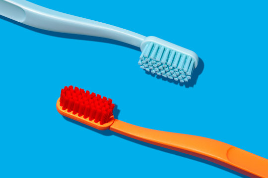 Modern Monochromatic Orange and Blue Toothbrushes Laying on Blue Background