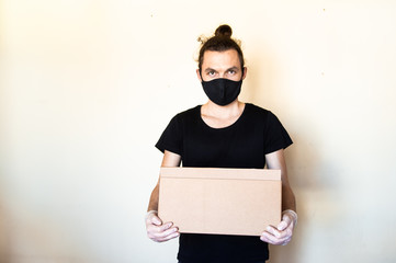A man wear protective face mask and gloves holding cardboard box. Delivery service and volunteering...