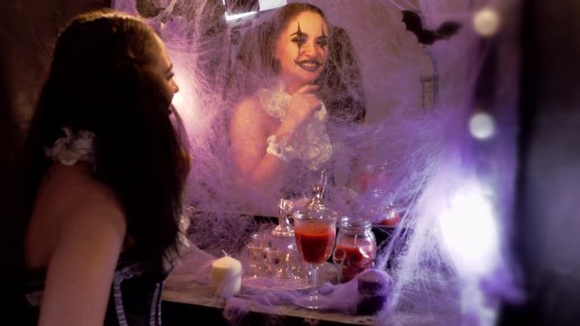 Portrait of a woman. Girl looks in the mirror. The mirror is decorated with cobwebs and bats. Model with makeup for Halloween. Woman flirting. The woman smiles at her reflection.