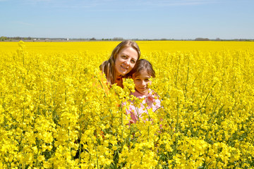Naklejka na ściany i meble Young woman with daughter stand in flowering rapeseed field