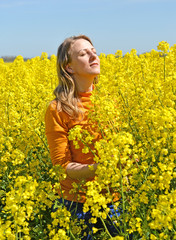 Naklejka na ściany i meble Portrait of a young woman with her eyes closed in a flowering rapeseed field