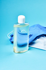 blank hand sanitizer with face mask and latex gloves over blue background. copy space. covid-19 symbol concept. vertical orientation.