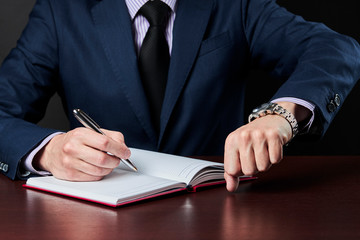 business plan and schedule concept. caucasian businessman write something at his diary and check time on a wristwatch.
