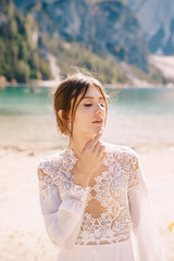 Fototapeta na wymiar Beautiful bride in a white chiffon dress with sleeves and lace on the shore of Lake Lago di Braies in Italy. Destination wedding in Europe, on the popular Braies lake.
