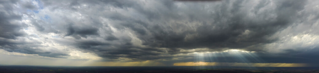 Panorama with a view of the rapidly approaching thunderstorm, the sun's rays shining through the...