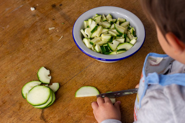 Very concentrated child cutting zucchini carefully not to cut himself