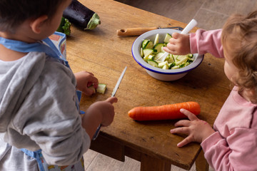 Two children, brother and sister, cutting vegetables to help their parents prepare dinner. helping at home during quarantine