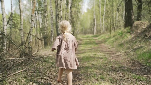 Little girl of two years old runs through the woods and turns around