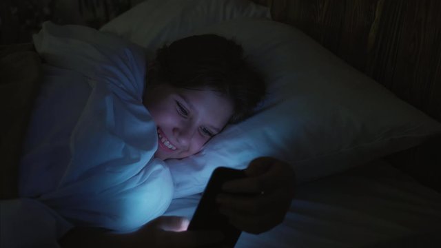 Teen leisure. Night Internet surfing. Girl scrolling app with memes on smartphone before sleep.