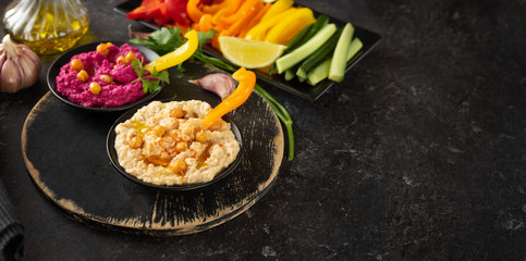 Variety of vegan hummus dips with colorful vegetable sticks on black background
