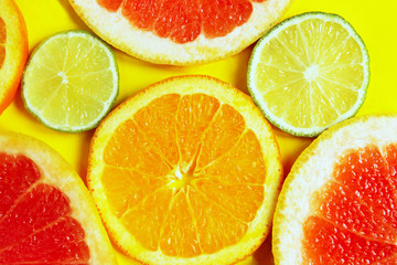 Sliced grapefruit, lime and orange are on yellow background. Colorful food background, horizontal view.