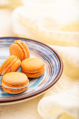 Orange macarons or macaroons cakes with cup of coffee on a white concrete background. Side view, selective focus.