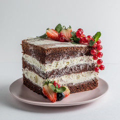 Slice of chocolate sponge cake on a white plate with cream and berries side view