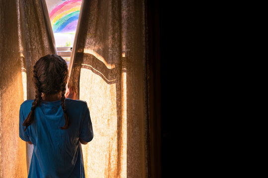 Young girl opening the curtains in a dark room to morning light and a painted rainbow