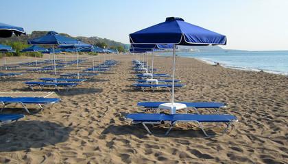 Blue umbrellas with sun beds on the sandy beach in Rhodes Faliraki