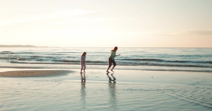 Kobieta z c&oacute;rką biegną wzdłuż  plaży o zachodzie słońca.