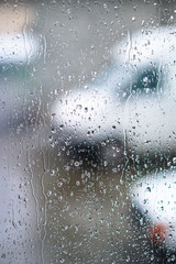 Window overlooking a rainy street. Gloomy evening weather with a view of the road. Drops on glass and bokeh from cars. Stock background for design