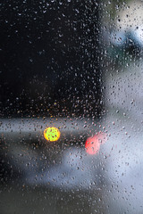 Window overlooking a rainy street. Gloomy evening weather with a view of the road. Drops on glass and bokeh from cars. Stock background for design