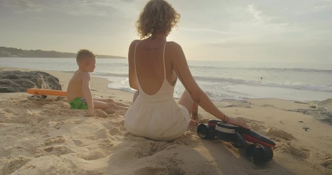 Boy with his mother sit on beach and looking at sea.