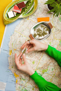 Hands in Green Sleeves Rolling Cannabis into Joints on Map of the West Coast