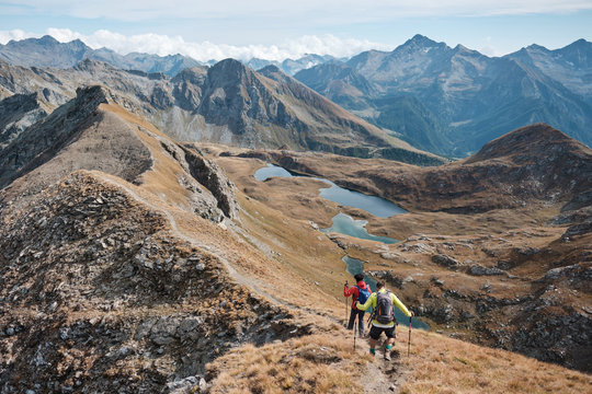 Two men walking on a panoramic trail in the alps with lakes as a background in a autumn sunny day